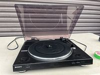 Front view of the Sony record player with dust cover open showing the platter, tonearm, and front left power button.