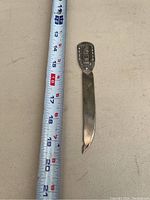 Full length photo of sterling silver letter opener next to measuring tape showing length about 7 inches.