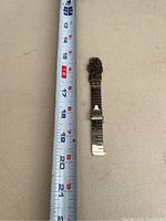 Full view of the sterling silver sewing ruler next to a tape measure showing a length of about 4.5 inches.