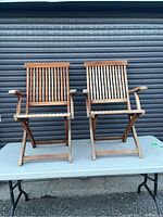 Two teak folding chairs placed on a table showing overall sun fading and outdoor wear.