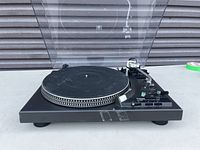 Front perspective of black Technics turntable with dust cover open, showing platter, tonearm and front tape residue