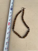 Photo shows tiger's eye bead necklace laid next to a measuring tape revealing length around 18 inches.