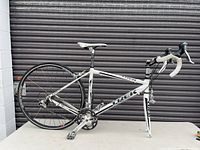 Full side view of Trek road bicycle on table showing frame, crankset, rear wheel, missing front wheel and fork leaning.