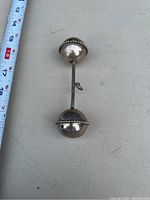 Photo of the Victorian baby rattle placed on a light surface next to a measuring tape showing size approximately 12cm.