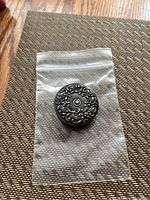 Photo of round compact Victorian sterling silver measuring tape in plastic bag on textured surface.