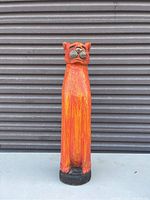 Photo of a tall, hand-painted, wooden carved cat statue in vibrant red and orange colors with black detailing on face and base.