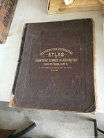 Front cover of atlas showing embossed brown binding with gilt lettering and decorative border