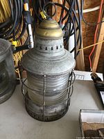Full view of ship’s lamp showing metal cage, clear glass globe and brass top with hanging loop