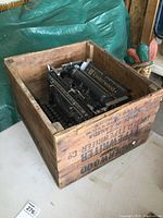 Antique Underwood typewriter in original wooden crate on table, visible crate markings on side.