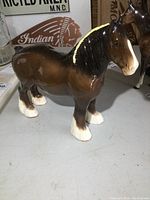 Front angled view of the brown ceramic horse figurine with light reflecting off the glossy surface, showing the white face and legs.