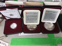 All three coins displayed in red velvet-lined boxes with accompanying information cards for the silver dollars.