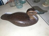 Side view of the wooden duck decoy showing detailed carved feather patterns, painted head with realistic eyes, and grey painted bill.