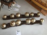 Photo showing two leather straps each fitted with 12 varying sized brass horse bells, arranged parallel on flat surface