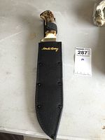 Hunting blade in sheath with embroidered brand.