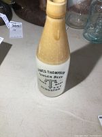 Full view of James Thompson Ginger Beer stoneware bottle showing the front print of the brand name, logo, and text on a white and brown glazed surface.