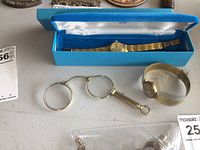Showing the gold-tone folding spectacles alongside two vintage ladies watches; one in a blue box with linked band, one with wide metal bracelet.