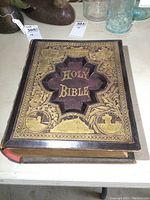 Front cover of large antique Bible showing detailed gold embossing and raised panel with 'HOLY BIBLE' text.