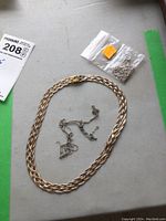 Overview of the four sterling silver chains including one large braided chain and three smaller chains in plastic bags on gray surface
