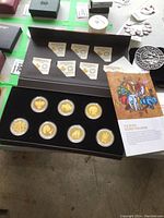 Display case opened showing all seven coins in capsules alongside seven certificates of authenticity and themed brochure.