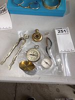 Lot items on table with plastic bags showing compasses, tongs, and watch band