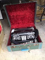 Open accordion in green case showing red velvet interior and black body