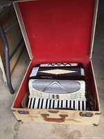 View of vintage Silvertone accordion inside open beige hard case with red felt interior, showing keyboard and grill.