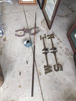 Overview of all weather vane parts including pole, brass letters, horseshoe base, and brass ball arranged on floor.