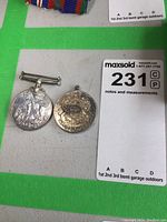 Pair of sterling silver Canadian war medals showing front sides placed on grey surface near lot number.