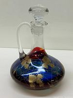 Full view of the Royal Danube decanter showing its broad base, narrow neck, clear handle and stopper, with abstract blue, red, and gold painted decoration.