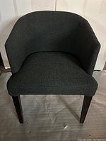 Front view of the gray fabric accent chair showing the upholstered seat, backrest, and dark wooden legs.