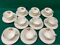 Overview of all ten tea cups and saucers arranged on a green cloth showing the set count and general condition.