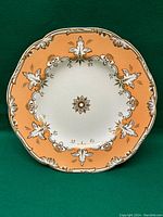 Top view of decorative plate showing pale orange border with gold and white Victorian designs and white center with gold flower motif.