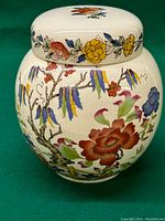 Front view of the ginger jar with lid showing colorful floral and tree design with berries and a fence.