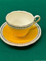 Front-top view of the yellow Aynsley teacup sitting on matching saucer showing cream interior and gold/black decorative trim.