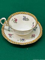 Full view of the Aynsley teacup placed inside the matching saucer, showing floral patterns and decorative striped rim.
