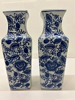 Front view of both blue and white vases showing detailed floral blue pattern on white base with square shape and flared necks.