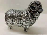 Front and side view of silver metal ram decor piece showing textured body and curled horns.
