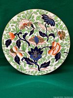 Full view of the round antique Coalport plate showing intricate hand painted florals and leaves in blue, green, and orange colors on white.