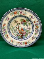Front view of the antique ceramic decorative plate with colorful floral and foliage design, showing intricate details and border pattern.