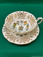 Top and side view of the porcelain tea cup with colorful Canada Coat of Arms and provincial shields, surrounded by gold decorative patterns.
