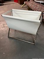 Front and side view of white leather magazine rack with stainless steel frame.