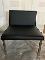 Front view of the black leather upholstered chair with stainless steel legs showing straight angular design and flat seat and backrest.