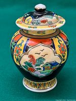 Front view of hand painted Japanese Kutani porcelain jar with vibrant floral and landscape motifs, lid in place.