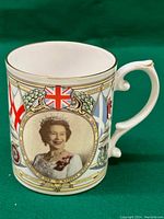 Full view of the commemorative mug showing the Queen Elizabeth portrait, British flags, and gold accents on porcelain.