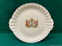 White scalloped ceramic dish against green background showing full front with coronation design.