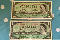Photo of the front side of two 1967 Canadian Centennial one dollar bills, placed on a blue surface with white polka dots.