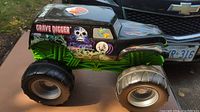 Side view of Grave Digger monster truck toy showing black body, large black tires, green chassis, skull and flame decals, and Chevrolet badge.