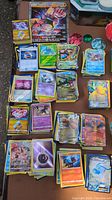 Stacks of Pokemon cards with various characters and energy cards visible, several collectible coins in multiple designs, and large holographic Buzzwole GX card.