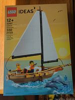 Front of the box showing assembled sailboat with large white sail, two minifigures on deck, two dolphins jumping in water, Lego Ideas branding and product details.