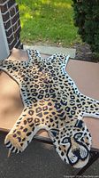 Full view of small leopard print rug laid flat on table outdoors showing full body shape including tail and head.